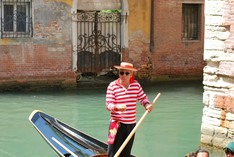 an old man wearing sunglasses and a straw hat stands on his boat in the canal