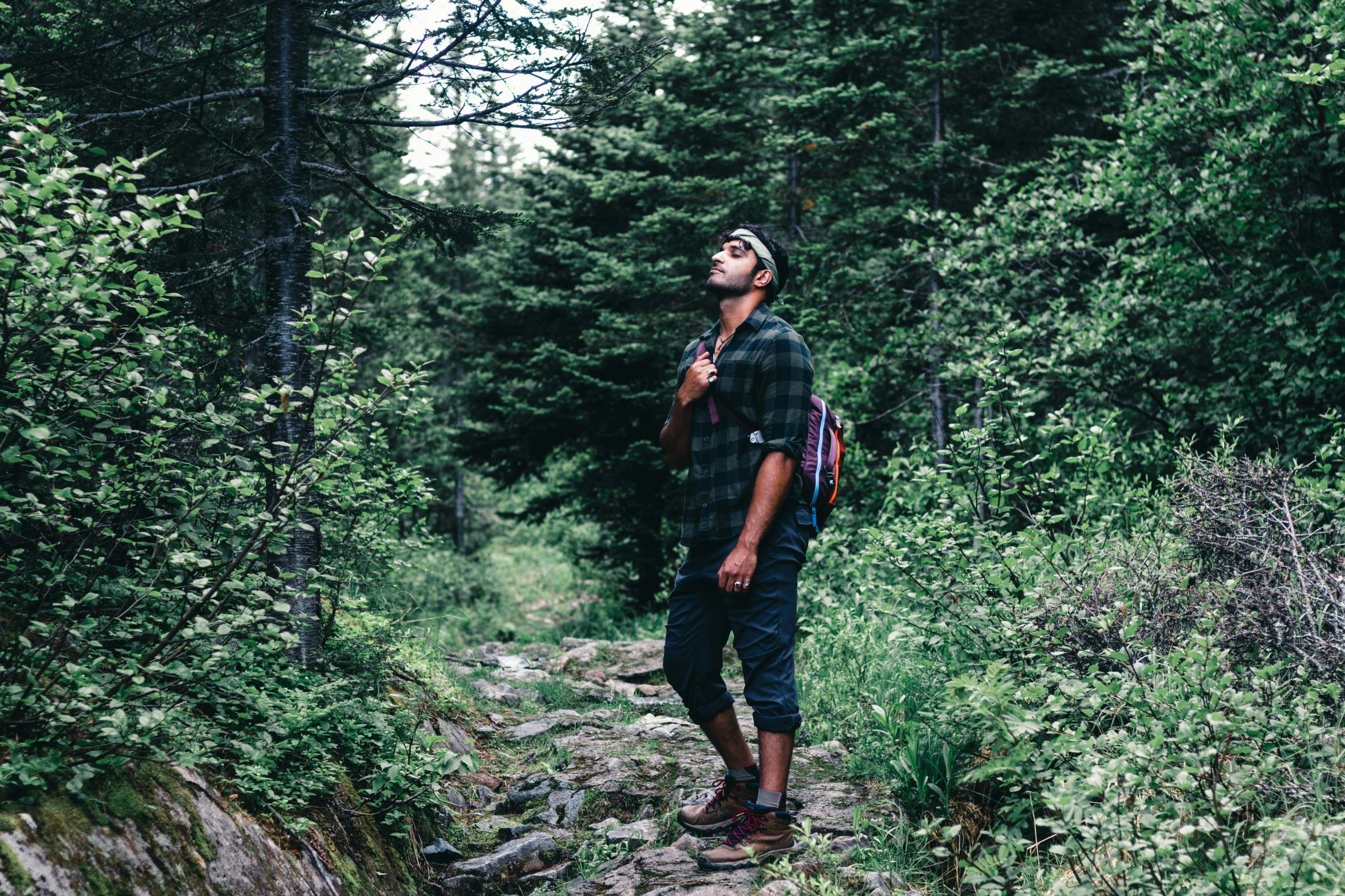 man in black shirt and hat standing on the side of a forest path