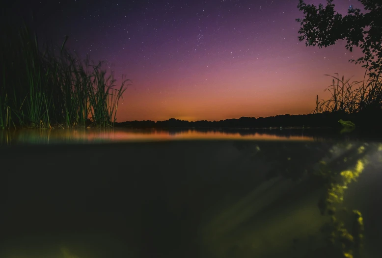 the night sky above the pond is bright, colorful and stars reflected in it