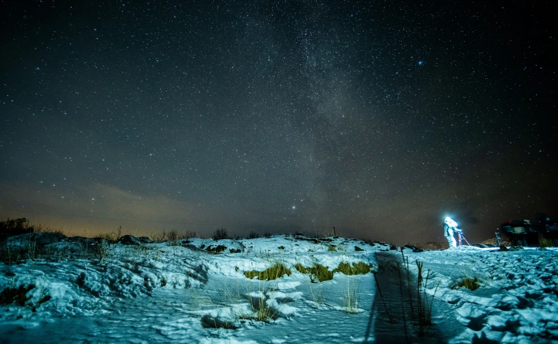 a night sky with stars and lights shines over a snowy hill