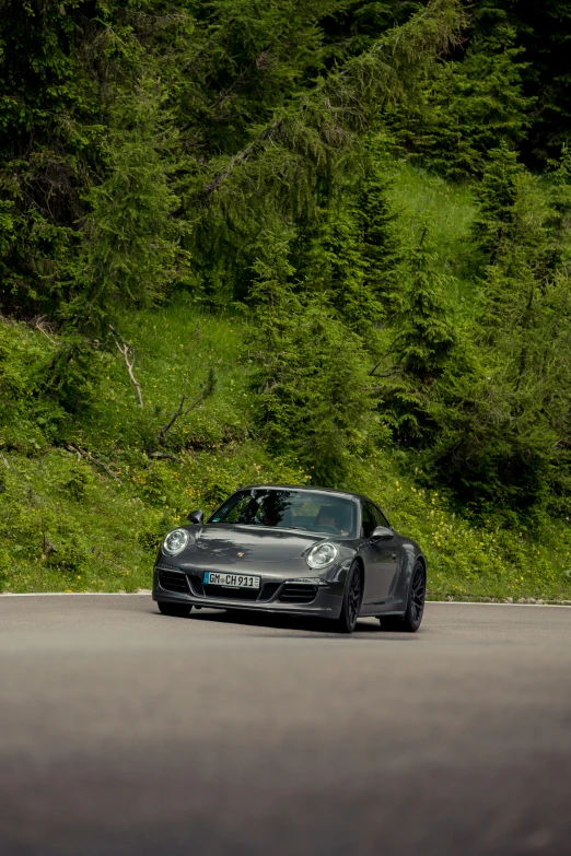 a gray sports car driving down a road next to lush green trees