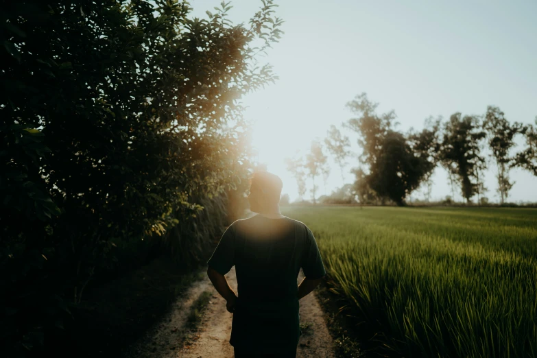 person standing on dirt path next to green field