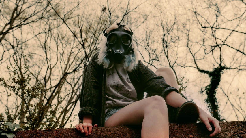 a man wearing a gas mask sitting on top of a rock