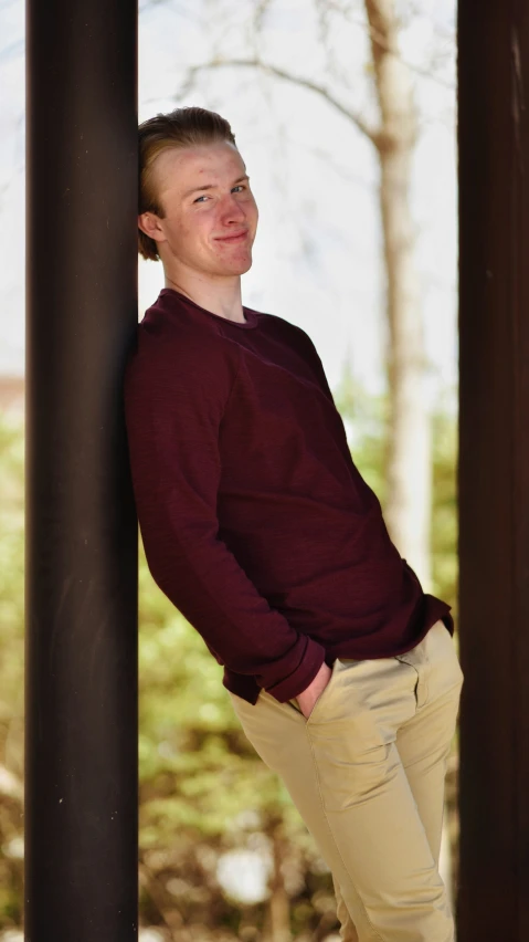 a man in tan pants leaning on metal pole