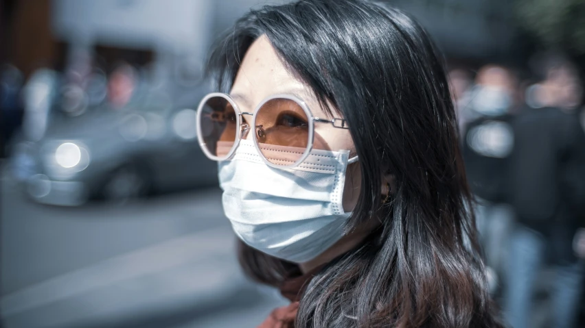 a woman with sunglasses wearing a mask on a city street