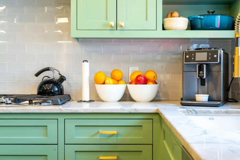 two bowls with fruit in them sit on a counter next to a kettle and coffee maker