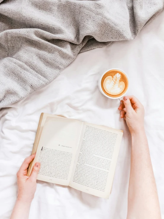 a woman laying on a bed and holding a book next to an open book