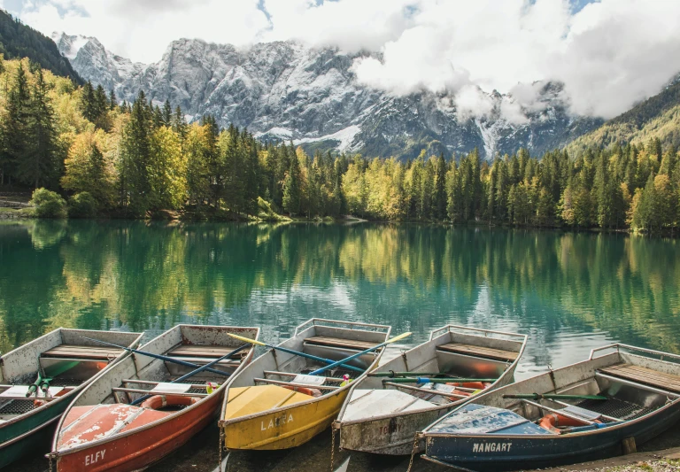 several different colored rowboats on the shore of a lake