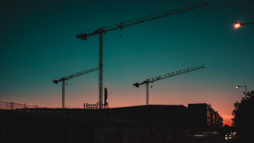 several construction cranes are silhouetted against the blue sky