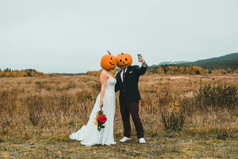 bride and groom with pumpkin masks take po in field