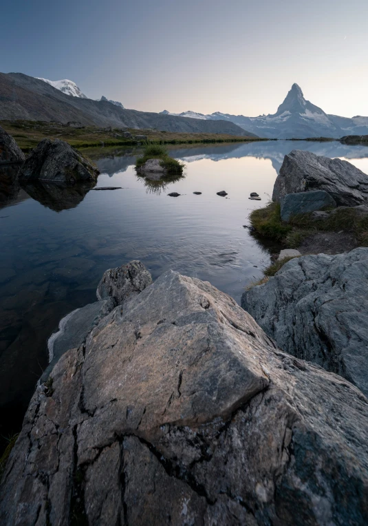 a lake surrounded by mountains with rocks and grass in the foreground