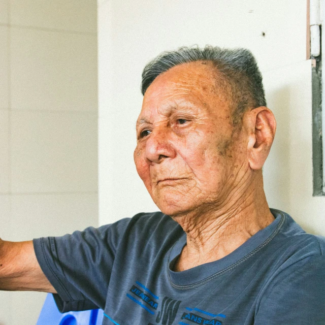 a man with gray hair and blue tshirt sitting with his arm in the air