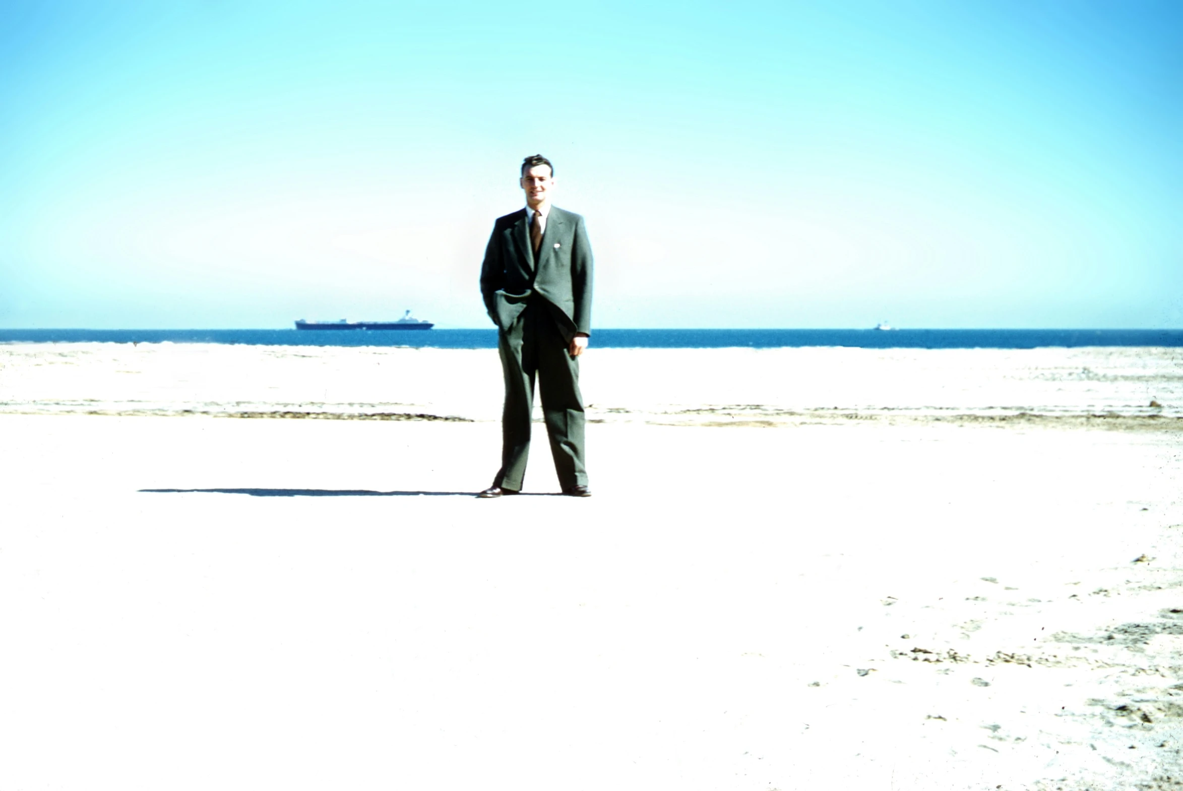 a man in business attire standing on beach next to ship