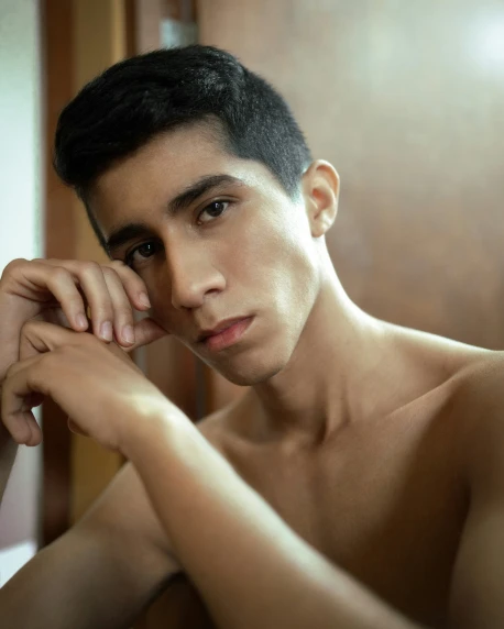 a shirtless male wearing glasses leaning against a mirror
