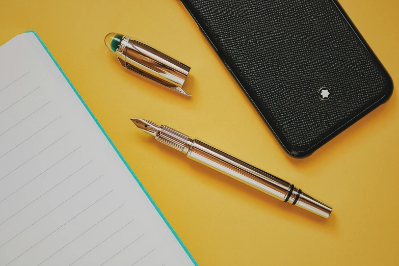 a cell phone on top of a notebook with two pen's