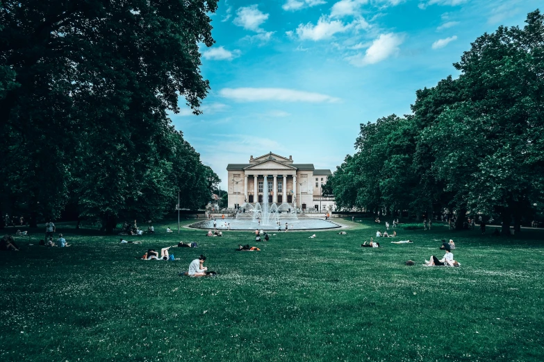 people are sitting around in the grass near a fountain