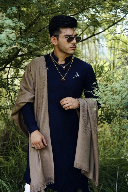 man with glasses on in a field of grass wearing a tan cardigan