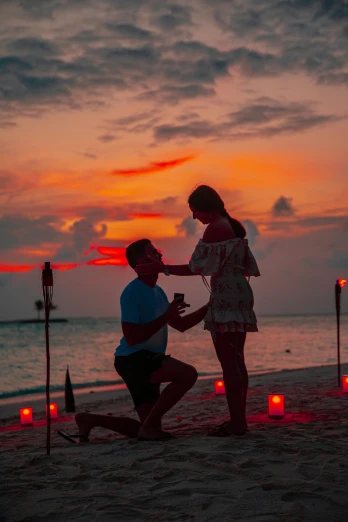 the woman and man are kneeling down in front of some candles on a beach