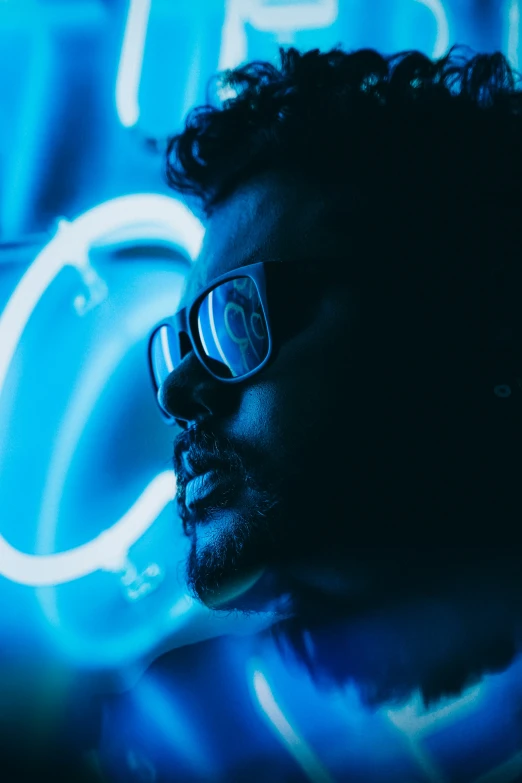 man wearing glasses with a neon sign in the background