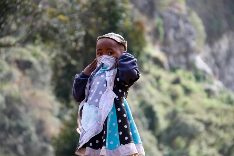 a little girl standing in the woods with a blue and white apron on