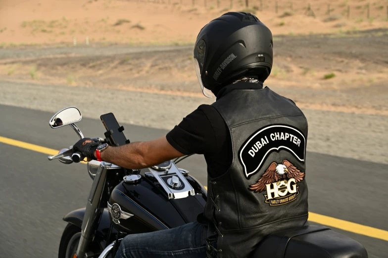 man in leather vest and helmet on motorcycle by the side of road