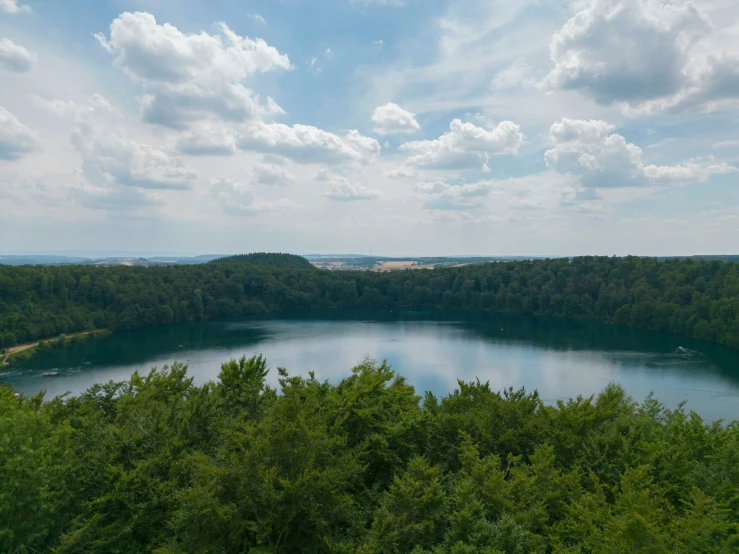 a large lake surrounded by forest under a cloudy blue sky