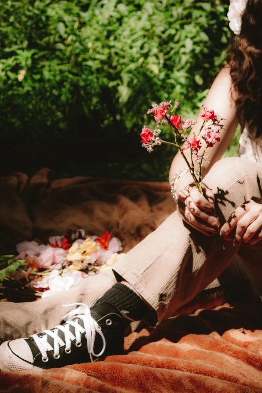 a woman sitting down and holding a plant with flowers in her lap