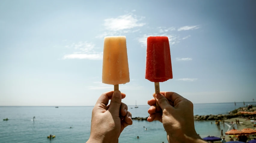 two hands hold colorful popsicles while over looking the water