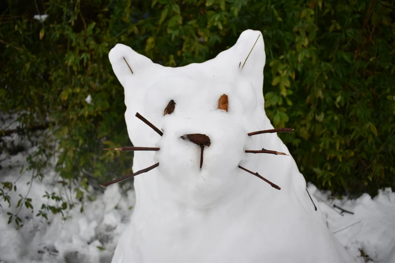 a statue of a cat is on snow in front of green bushes