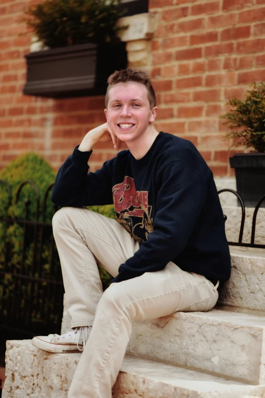 a young man wearing a sweater sitting on some steps