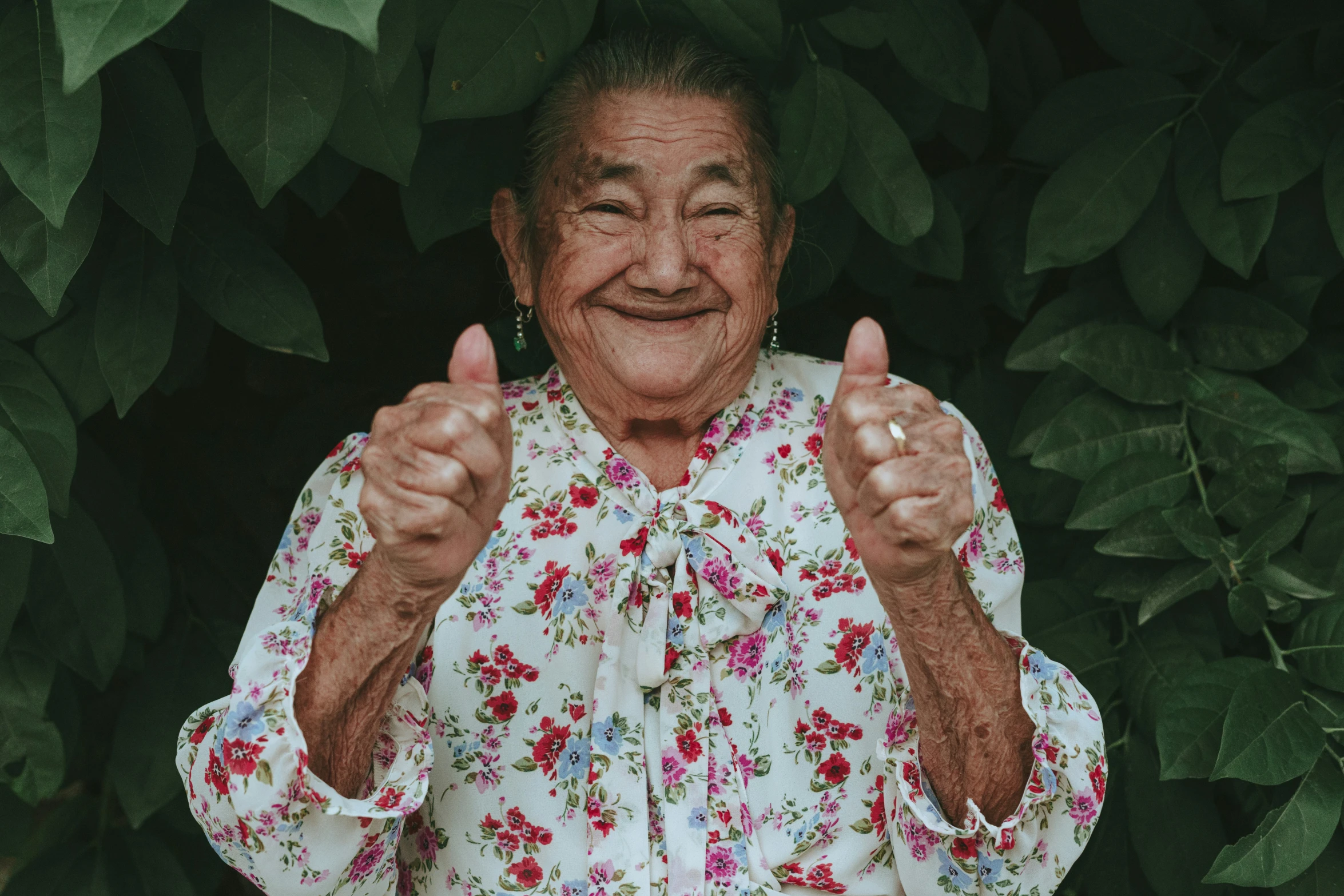 an older woman with thumbs up in front of some plants