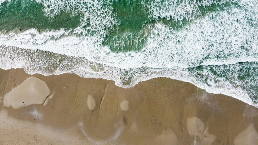 an aerial view of a beach with surf and a few small rocks