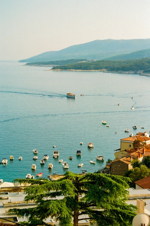 small boats traveling on the water near houses and hills