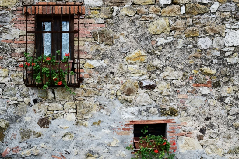 two windows on the side of a stone wall and a window with brown bars
