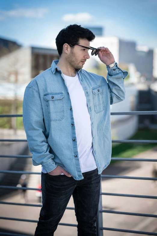 a man in jeans is leaning against the fence with his hand on his head