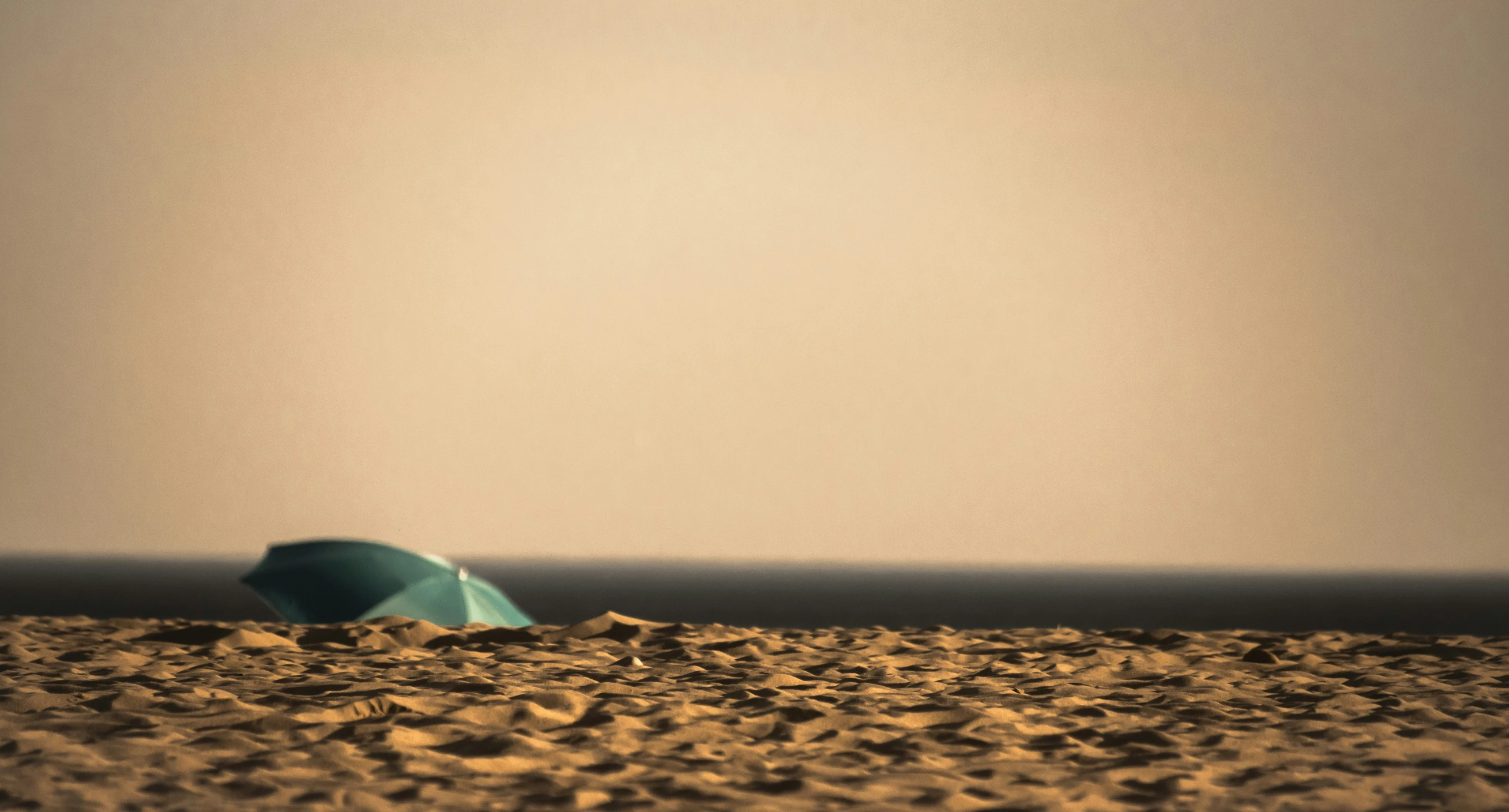 a blue umbrella is on the beach in the sand