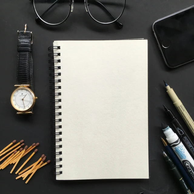 an open notebook next to a watch and glasses