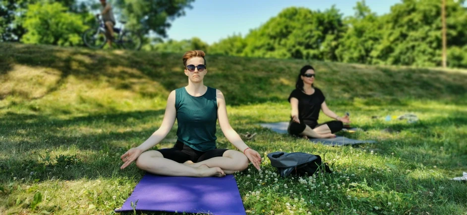 two women doing yoga in the park on yoga mats