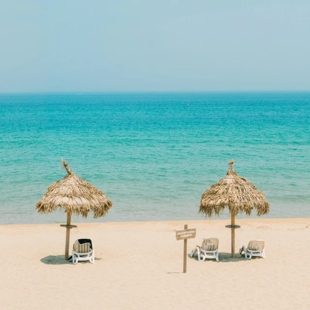 two straw umbrellas sit near chairs on a beach