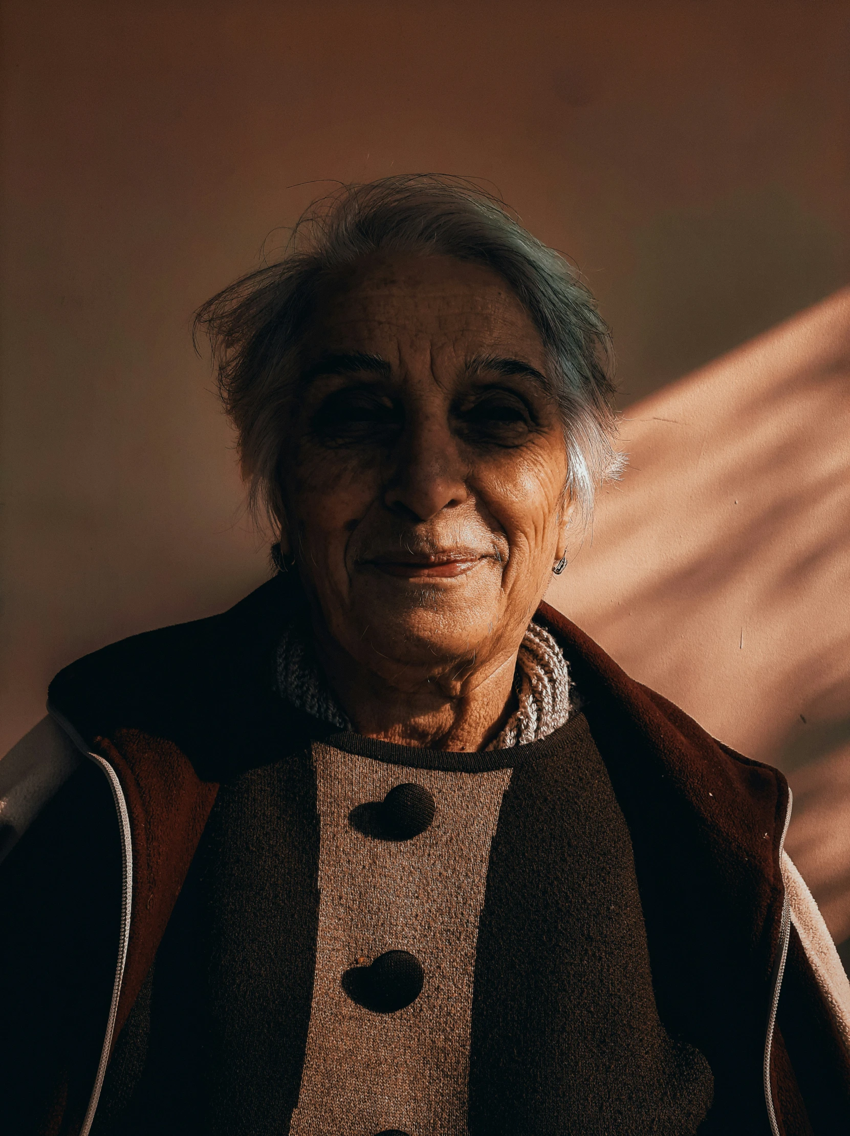 an older woman smiles as she stands near a wall