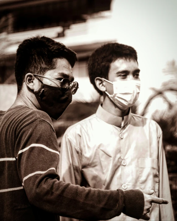 two young men, one wearing a face mask and one holding a glass