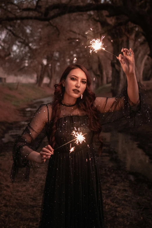 a woman holding sparklers standing under a tree