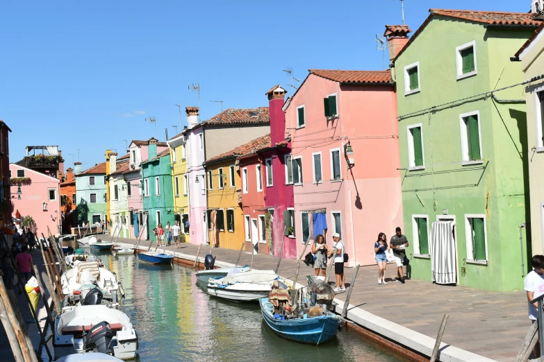 people are walking on the side of a canal that is lined with boats