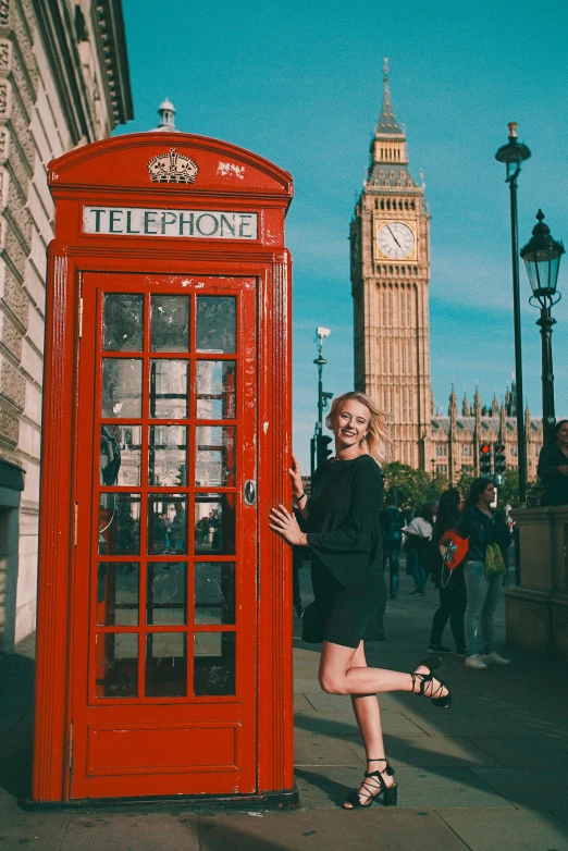 a woman is posing in front of a red phone booth