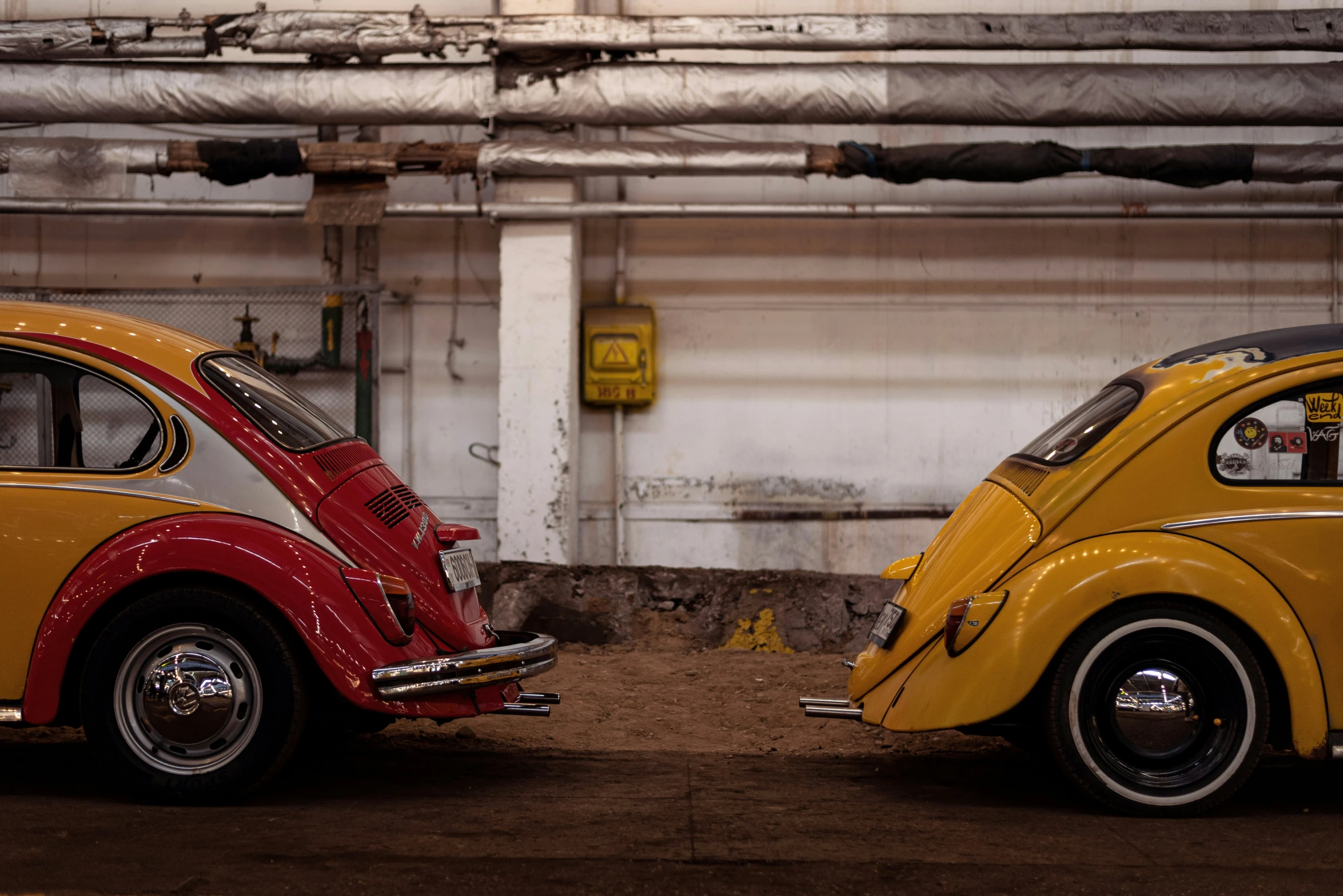 two antique beetle - type cars parked side by side in a garage