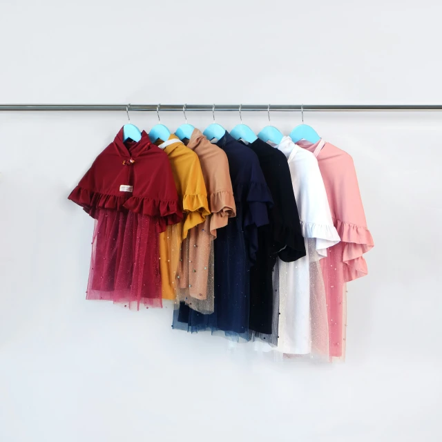 several colored dresses hang on a wire against a white wall