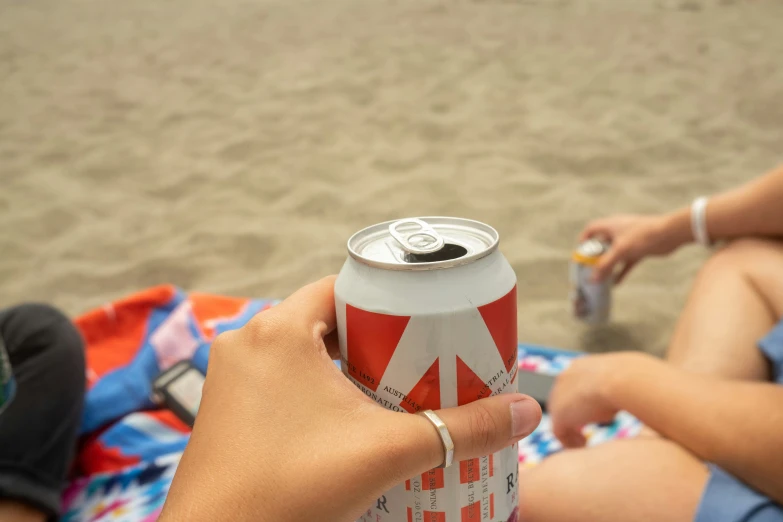 a person holding a soda can with another hand while sitting on the beach