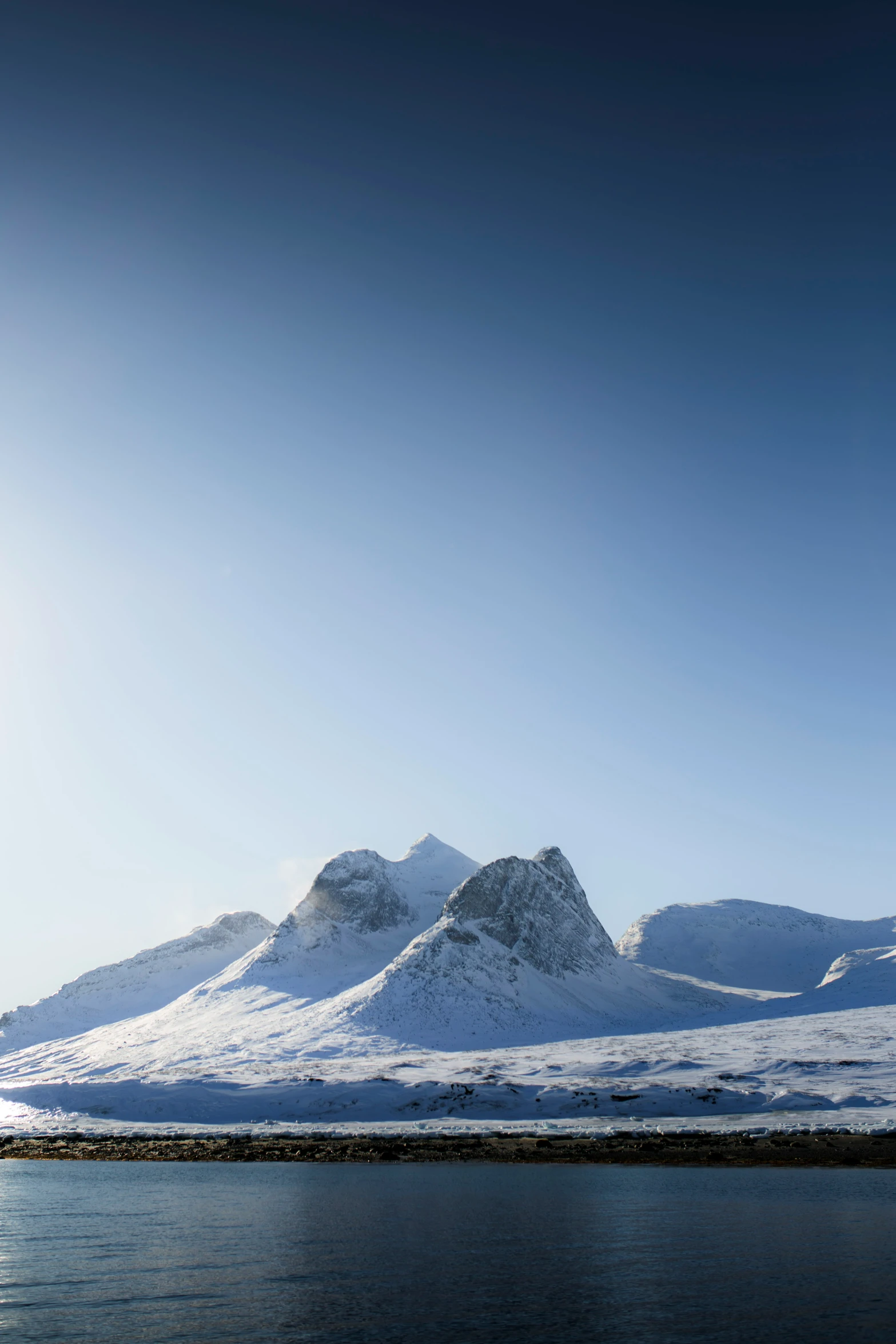 snow covered mountains near the ocean under a clear blue sky