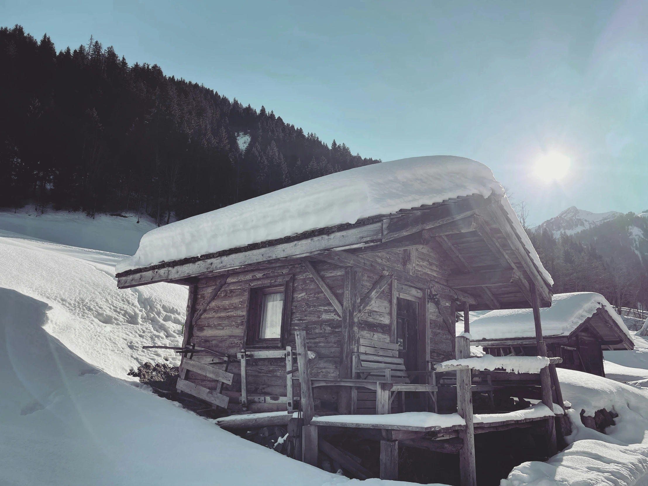 a hut with porches and a small fence is covered in snow