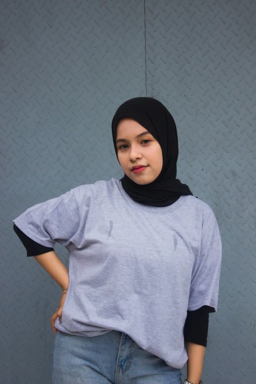 a women wearing jeans and a grey top is standing against a gray background